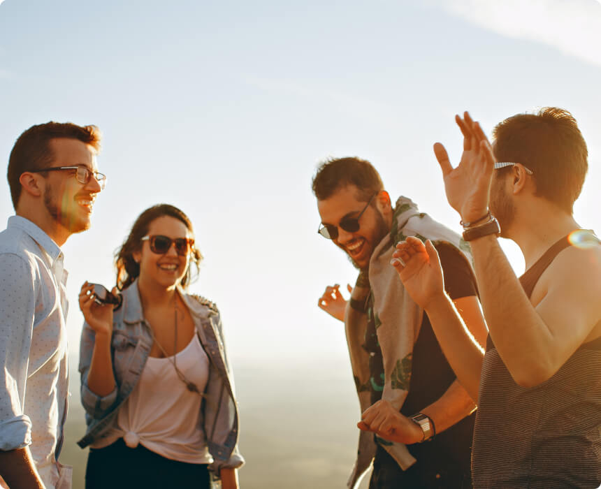 Group of friends standing outdoors at sunset, laughing and talking together, enjoying relaxed conversation under a clear sky.