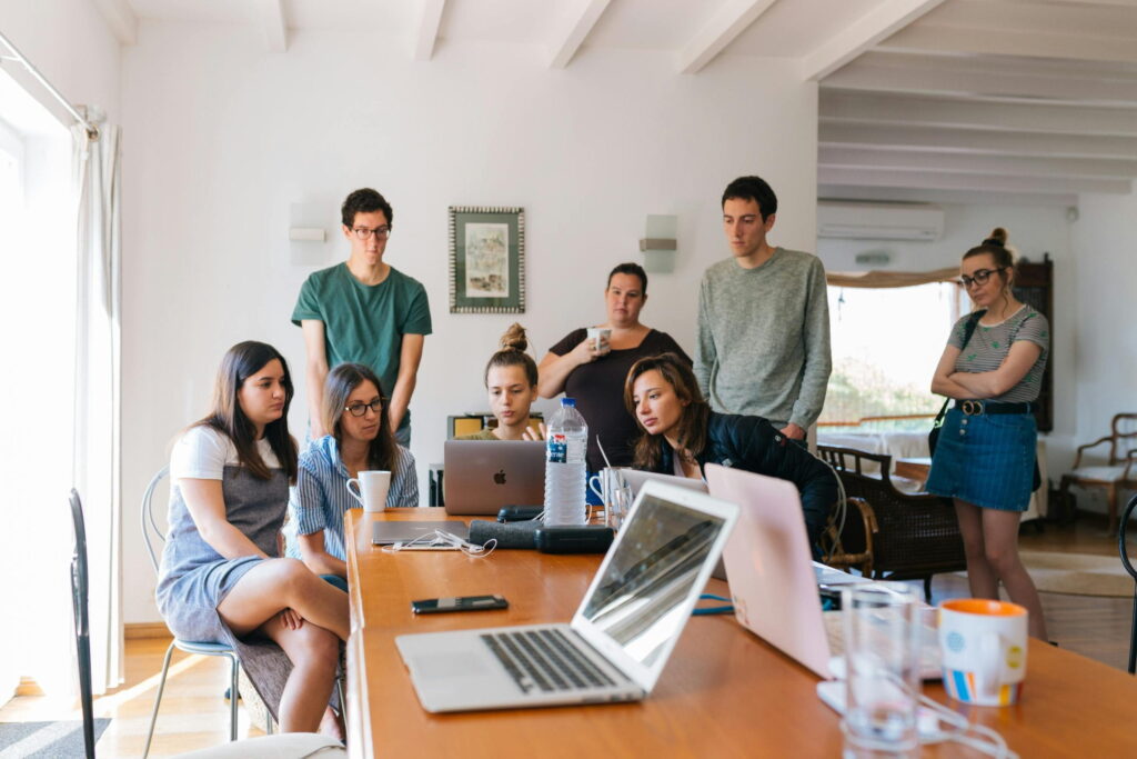 Group of young professionals gathered around a table with laptops and coffee, collaborating during an informal meeting in a bright modern workspace.